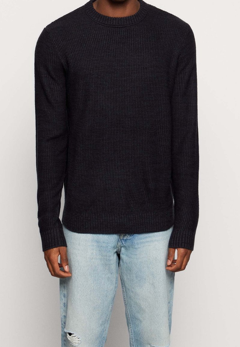 Marinblå ribbstickad tröja med rund halsringning och långa ärmar. Kombinerad med ljusblå slitna jeans, som visar en avslappnad passform.