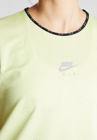 Detailní záběr osoby, která má na sobě světle zelené tričko Nike Air s černým límečkem, na kterém se opakuje text "AIR".