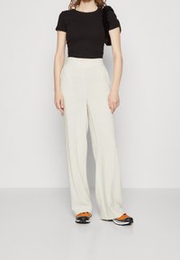 Camiseta negra de corte cropped y pantalones de lino beige claro de pierna ancha, combinados con zapatillas negras y naranjas. Tejido texturizado y diseño sencillo.