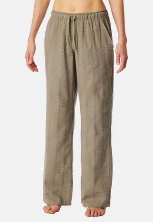 Väljässä istuvia, beigejä, teksturoiduista kankaista valmistettuja housuja, joissa on joustava kiristysnyöri vyötäröllä, paljain jaloin seisovan henkilön päällä.