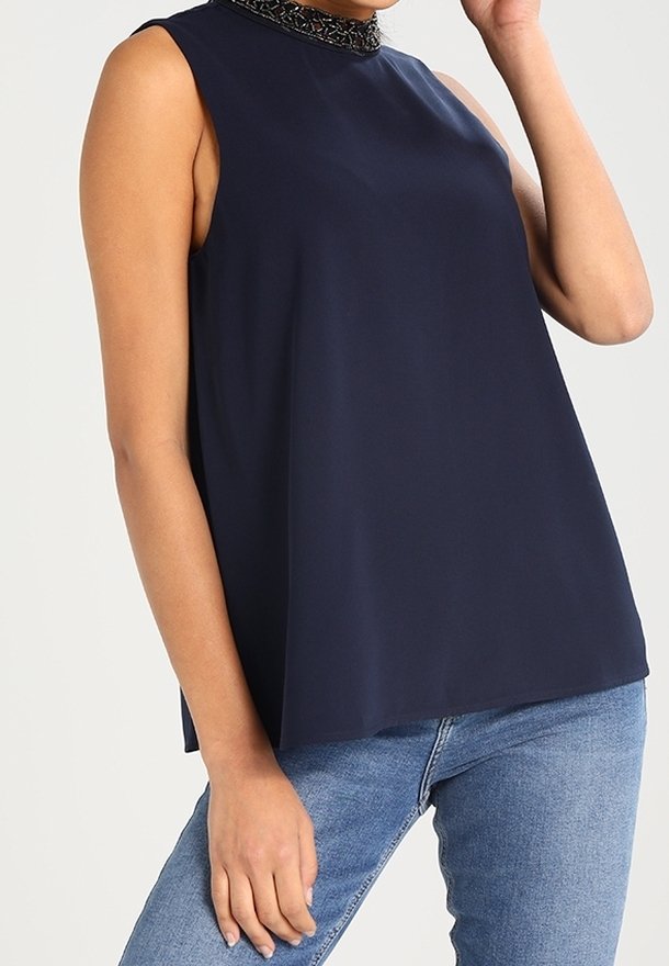 Haut sans manches bleu marine avec un col haut, orné d'un collier à perles décoratives, fabriqué en tissu léger ; design ample.