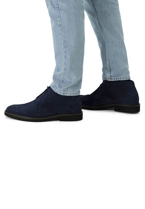 Marineblauwe suède enkellaarsjes met een ronde neus en een minimalistisch vetersluiting, gecombineerd met lichtblauwe tapered jeans, met een soepele zwarte zool.