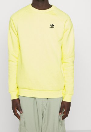 Felpa fluorescente gialla con maniche lunghe a raglan. Presenta un logo Adidas nero sul petto sinistro e un orlo a costine. Tessuto morbido.