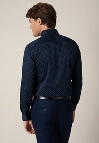 Granatowa koszula z długim rękawem z małymi białymi wzorami, z klasycznym kołnierzem i mankietami na guziki, w zestawie z ciemnymi spodniami i skórzanym paskiem.