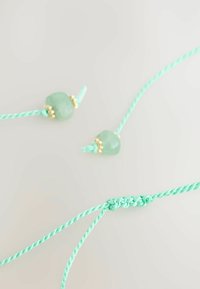 Ett ljust mintgrönt makraméarmband med två släta, runda pärlor och guldaccenter, med en flätad textur och justerbar design.