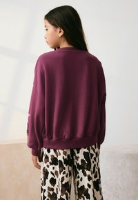 Sweatshirt violet cu manșete și tiv cu nervuri, asortat cu pantaloni evazați cu imprimeu animalic în culori negru și maro. Țesătură moale, croială relaxată.