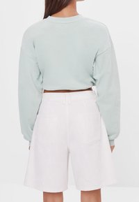 Světle zelená zkrácená mikina s dlouhými rukávy spárovaná s bílými denimovými šortkami do poloviny stehna. Tento outfit má volný střih a minimální detaily.