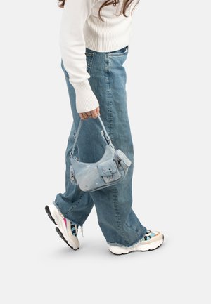 Borsa a mano di stoffa morbida blu chiaro con forma arrotondata, tasca frontale e dettagli metallici. Indossata con jeans larghi e sneakers.