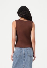 Haut en tricot sans manches de couleur marron, avec un col rond, une coupe ajustée et une texture côtelée. Associé à une jupe en denim dotée de poches à l'arrière.
