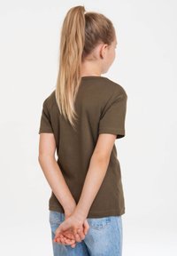 Camiseta de manga corta en verde oliva con un escote redondo, hecha de algodón suave, combinada con jeans de mezclilla azul claro. Vista trasera, manos juntas.