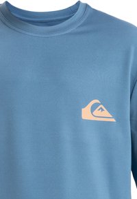 Blå långärmad skjorta i mjukt material med en rosa logotyp på vänster bröst. Rund halsdesign med en slät yta.