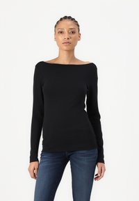 Maglietta nera a maniche lunghe con scollatura off-the-shoulder, design aderente e texture liscia. Abbinata a jeans in denim blu.