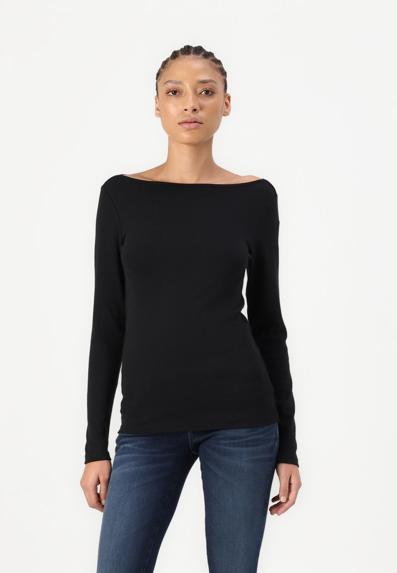 Maglietta nera a maniche lunghe con scollatura off-the-shoulder, design aderente e texture liscia. Abbinata a jeans in denim blu.