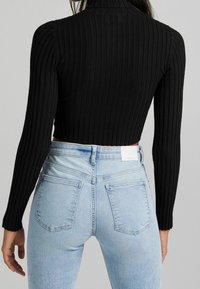 Svart ribbad långärmad croppad topp i kombination med ljusblå högmidjade jeans med tre fickor och subtil slitning.