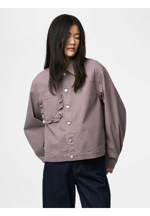 Žena s dlouhými tmavými vlasy, oblečená v lehkém proužkovaném sáčku se stříbrnými knoflíky a kapsou s volánky, doplněném tmavě modrými džínami.