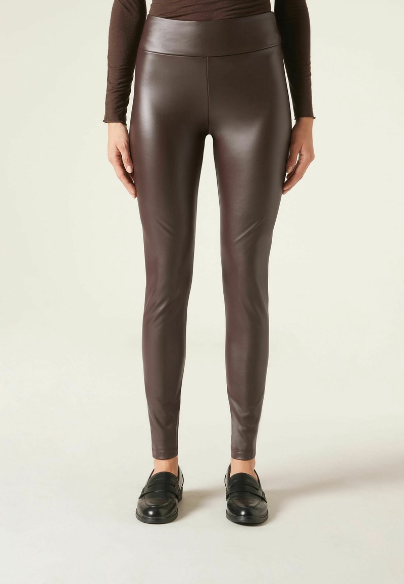 Bruine neplederen legging met een hoge tailleband, slim fit, gladde textuur en minimale details, gecombineerd met zwart instap-schoenen.