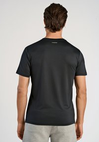 Svart kortärmad t-shirt gjord av slät tyg, med rund hals och en liten logotyp nära halsringningen.