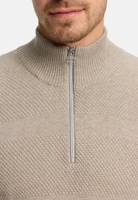 Beige halvdragna tröja i texturerat stickat tyg, med ribbad krage och en slät dragkedja med metallisk detaljer.