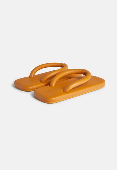 Oranssit flip-flopit, joissa on litteä, suorakulmainen pohja ja kaksinkertaiset kaarevat nauhat, jotka on valmistettu sileästä kumimateriaalista. Ei näkyviä kuvioita tai aksentteja.