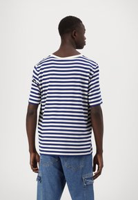 Camiseta de rayas en azul y blanco, con cuello redondo y mangas cortas. La vista posterior revela un corte relajado y una textura suave.
