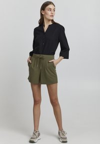 Svart långärmad skjorta med v-ringning och knappar, kombinerad med olivgröna shorts med elastisk midja och fickor.