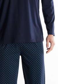 Marineblaues Langarmshirt kombiniert mit gemusterten Schlafanzughosen, die ein Wabenmuster in dunklerem Blau und türkisfarbenen Punkten aufweisen. Sanfte Stofftextur.