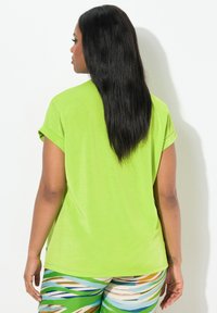 Top a maniche corte, verde lime, con vestibilità rilassata, caratterizzato da orli arrotolati e una texture liscia, abbinato a pantaloni corti multicolore e fantasia.
