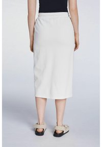 Jupe midi blanche avec une taille élastique, texture lisse et ourlet simple. Associée à des sandales duveteuses avec des accents de boucle.