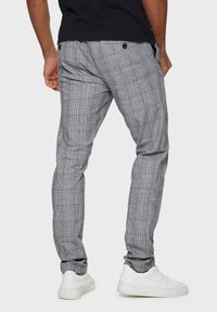 Pantaloni a quadri grigi realizzati in tessuto leggero, caratterizzati da una vestibilità slim, vita elastica e due bottoni sul retro. Abbinati a sneaker bianche.