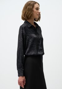 Black satin blouse with a floral design, featuring a collar, long sleeves, and buttons down the front; smooth texture and elegant silhouette.