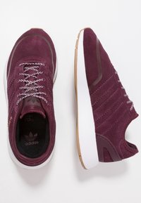 Maroon suede athletic shoes with white rubber sole, textured laces, and gum rubber accents. Features logo on tongue and side.