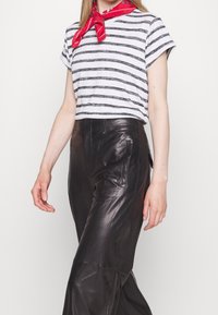 Personne portant un t-shirt rayé blanc et noir, un foulard rouge autour du cou et un pantalon en cuir noir taille haute.