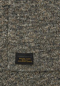 Gebreide stof in grijstinten met oranje en witte accenten. Beschikt over een zwarte label met de tekst "camel active" en "MADE FOR DAILY ADVENTURES."