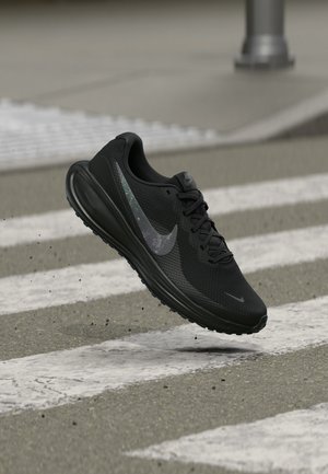 Musta Nike juoksukenkä ilmassa suojatien yllä kadulla, kengän ympärillä pieniä irtonaista roskaa.
