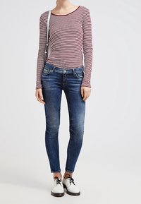 Top de manga larga a rayas rojas y blancas, jeans ajustados azul, y zapatos de cordones en blanco y negro, con un bolso cruzado delgado.