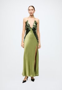 Halter-neck evening gown in olive green satin, featuring sequin detailing on the bodice and a thigh-high slit on one side. Black heels.