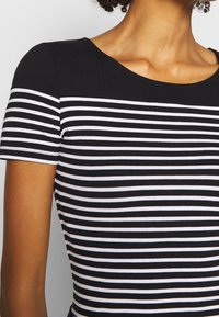 Camisa a rayas en blanco y negro con mangas cortas. Tela suave y elástica. Cuello redondeado, con rayas horizontales de anchos variados.