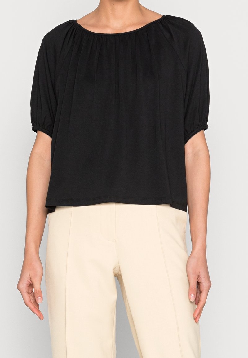 Sort top med korte ærmer, løs pasform og samlet halsudskæring. Lavet af blødt stof, med pufærmer og lige kant.