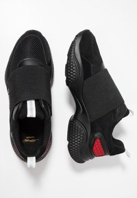 Schwarze Sportschuhe mit einem Obermaterial aus Mesh, elastischem Riemen über dem Mittelfuß, strukturiertem Fersenbereich und roten Akzenten. Strapazierfähige Gummisohle mit Grip-Muster.