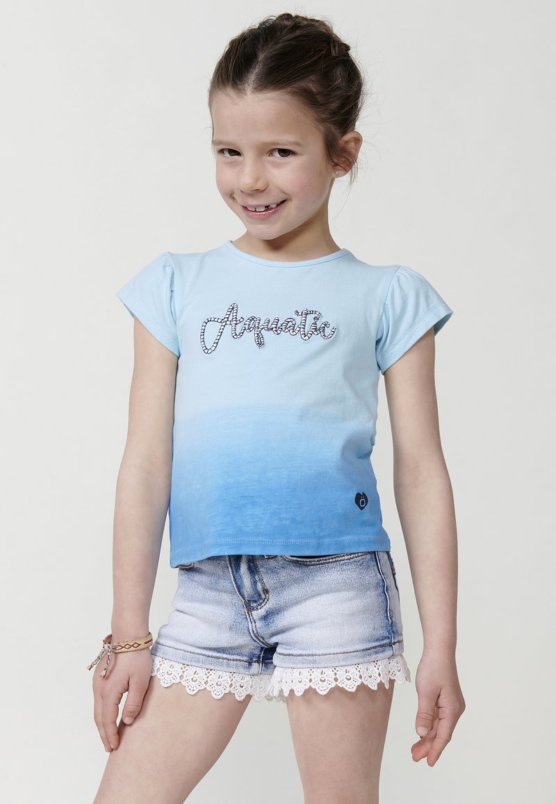 Svetlo modra kratka majica s kratkimi rokavi z gradientom od svetle do temnejše modre, z napisom "Akvatično" v rhinestones. V kombinaciji z denim kratkimi hlačami z čipkastim robom.