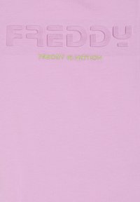 Camiseta de algodón rosa claro con texto en relieve "FREDDY" y bordado "FREDDY IS MOTION" en verde neón debajo.
