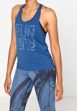 Nainen sininen hihaton juoksupaita, jossa teksti "RUN", ja siniset kuviolliset legginsit, seisoo yksinkertaista valkoista taustaa vasten.