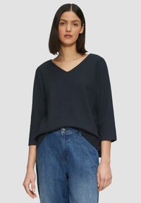 Camicetta blu navy con scollo a V e maniche a tre quarti, abbinata a pantaloni in denim azzurro chiaro. L'outfit presenta una vestibilità morbida e un design semplice.