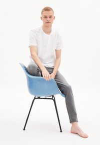 Blue molded plastic chair with black metal legs; seated figure in a white t-shirt and gray jeans, barefoot. Simple background.