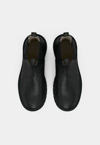 Černé kožené nazouvací boty s texturovaným povrchem, zaoblenou špičkou a gumovou podrážkou. Mají elastické boční panely a poutka pro snadné nazouvání.