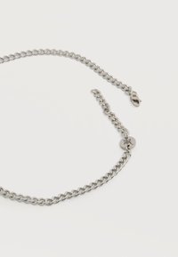 Ασημένιο κολιέ αλυσίδας με διασυνδεδεμένους κρίκους και μικρό στρογγυλό κούμπωμα με διακριτικό χαραγμένο σύμβολο, παρουσιάζεται σε απλό λευκό φόντο.