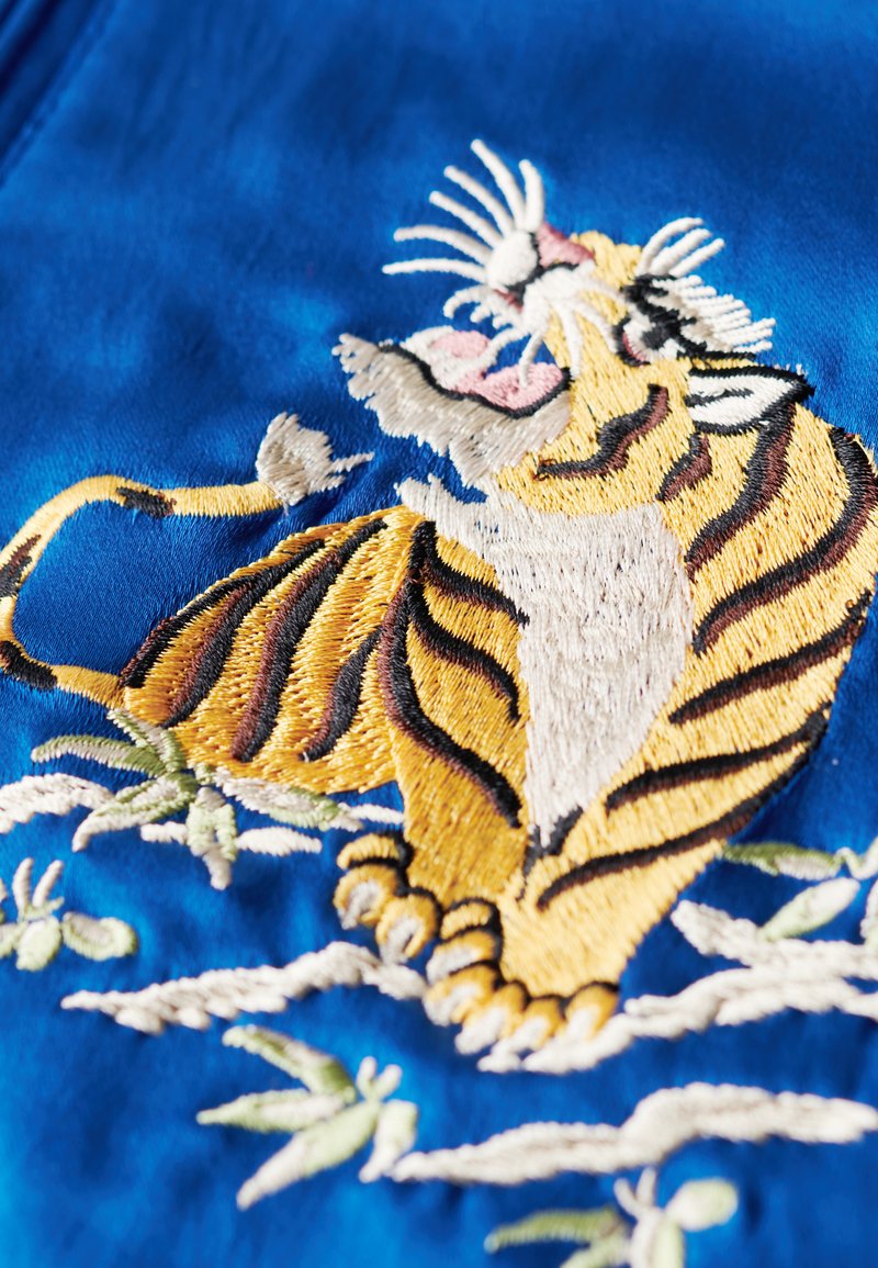 Patch brodé représentant un tigre jaune et noir sur fond de soie bleue, avec des accents de bambou verts et des détails blancs.