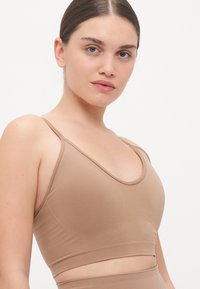 Svetlo béžová bezšvová bralette s kulatým výstrihom, tenkými nastaviteľnými ramienkami a priliehavým pásom. Vyrobená z mäkkého, elastického materiálu.
