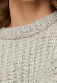 Vaaleanharmaa neulottu villapaita, jossa on resorikauluksen yksityiskohta, pehmeä tuntuma ja paksu kudontakuosi.