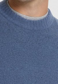 Pull tricoté bleu avec un col rond côtelé, fabriqué en matière douce et texturée, présentant un motif chiné subtil.